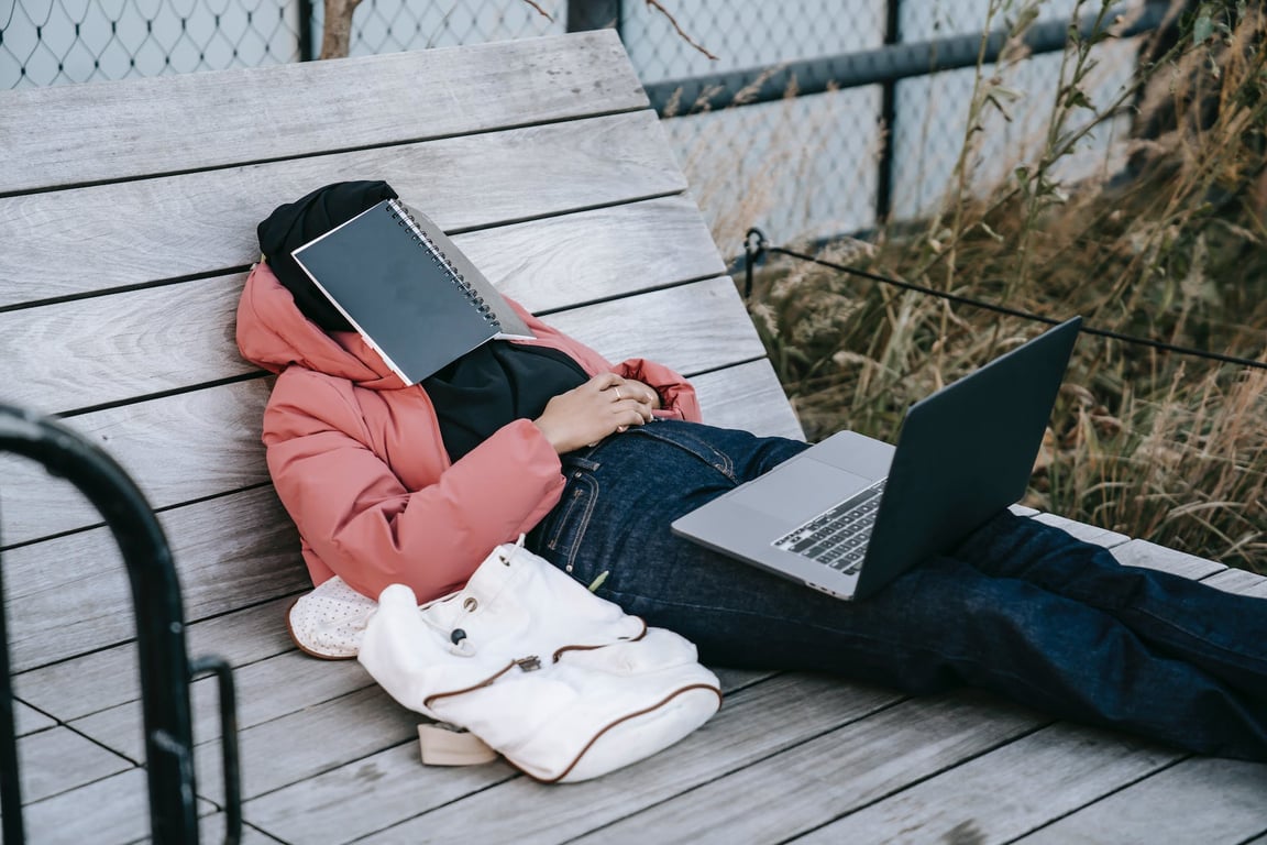 Femme méconnaissable avec un ordinateur portable se reposant sur un banc dans un parc